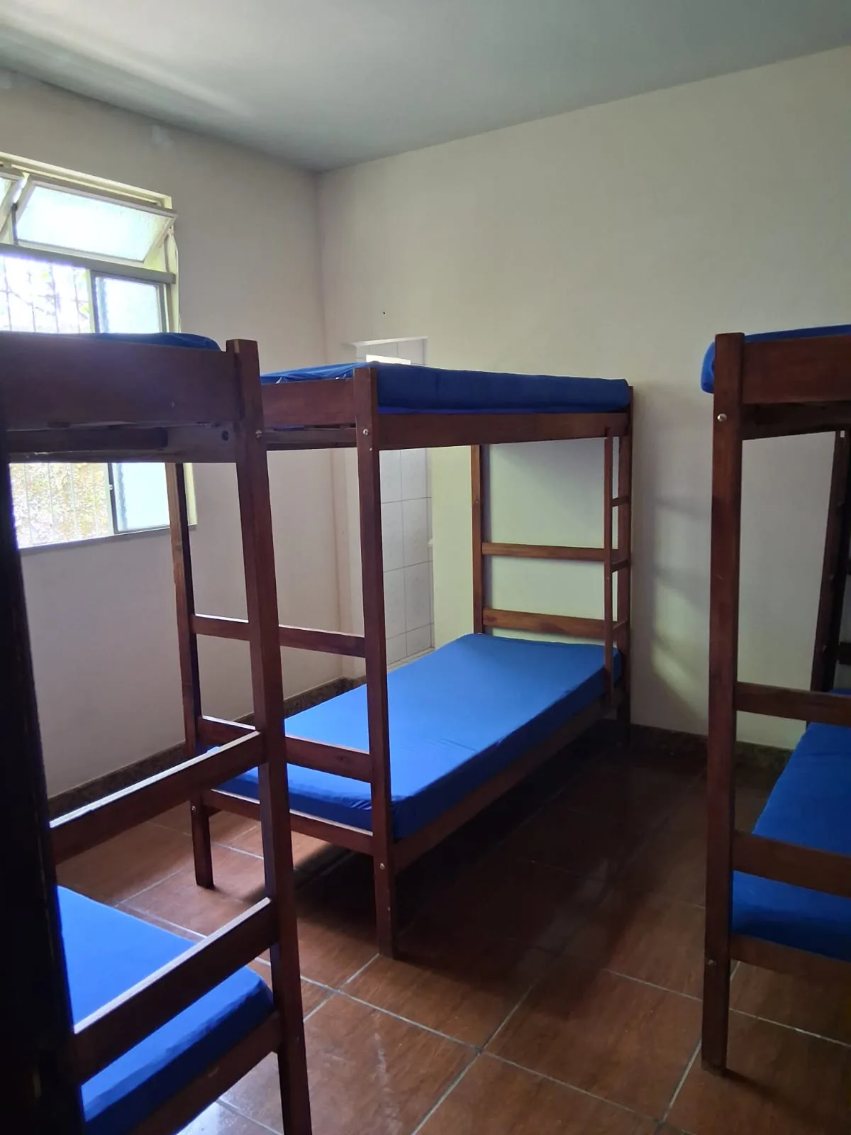 Quarto com beliches de madeira, colchoes e piso ceramico.